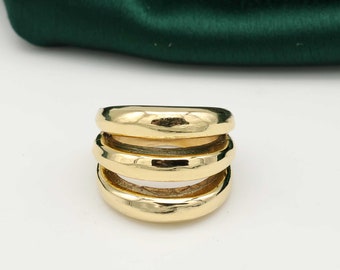 Può includere: Un anello dorato dal design impilato. L'anello presenta tre fasce arrotondate, creando un look audace e moderno. La superficie lucida riflette la luce, evidenziando la consistenza liscia. Questo gioiello è adatto all'uso quotidiano.