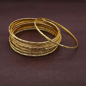 May include: A set of eight gold-toned bangles with an intricate floral design. The bangles are stacked on top of each other.