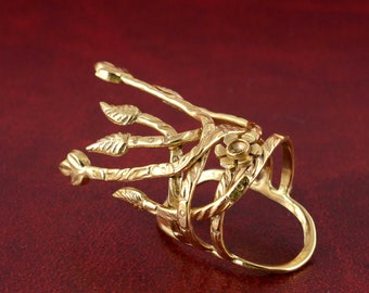 Op de afbeelding: Een gouden ring met een bloemmotief. De ring is gemaakt van meerdere banden die met elkaar zijn verweven en een bloemmotief hebben. De ring heeft een bloemmotief aan de bovenkant.