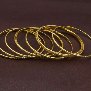 Puede incluir: Un conjunto de diez pulseras doradas con un diseño texturizado. Las pulseras están apiladas unas sobre otras.