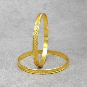 May include: Two gold bangles with a chevron pattern. The bangles are stacked on top of each other.