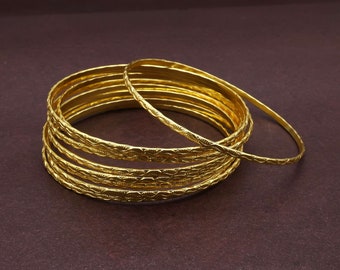 May include: A set of eight gold-toned bangles with intricate etched designs. The bangles are stacked on top of each other.