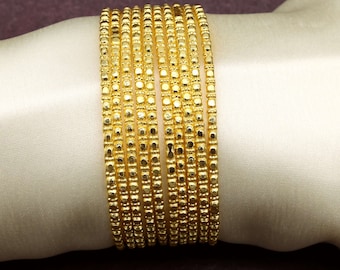 May include: A set of ten gold bangles with a textured, beaded design. The bangles are stacked on top of each other.