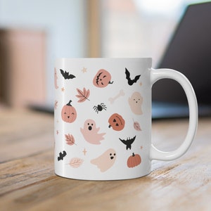May include: White ceramic mug with a Halloween-themed design. The mug features a pattern of ghosts, pumpkins, bats, spiders, and stars in shades of pink and black.