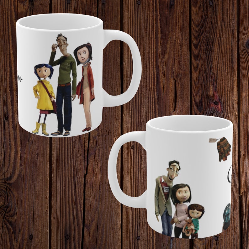 May include: Two white ceramic mugs featuring a colourful illustration of a family from the film "Coraline" printed on them. The mugs are on a wooden background.