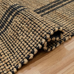 以下が含まれることがあります： 黒と茶色の織り模様が施された天然繊維の敷物のクローズアップ。敷物は折り畳まれており、織りの質感とディテールがわかります。