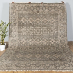 May include: A large, rectangular rug with a beige and gray geometric pattern. The rug has a fringe border.