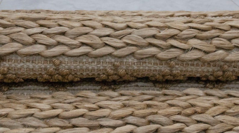 May include: Close-up of a woven rug made of natural fibers. The rug has a braided texture and a light brown color.