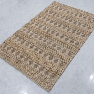 May include: A natural fiber rug with a woven diamond pattern in beige and brown tones. The rug has a textured surface and is made of natural materials.