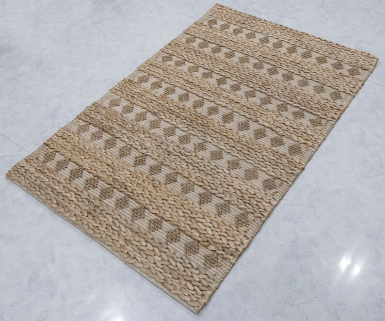 May include: A natural fiber rug with a woven diamond pattern in beige and brown tones. The rug has a textured surface and is made of natural materials.
