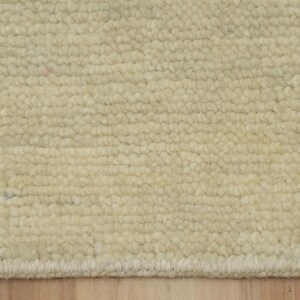 May include: A cream-colored rug with a dense, looped pile texture. The surface features a consistent, uniform pattern of small, rounded loops arranged in horizontal rows, creating a tactile and soft appearance across the entire visible area.