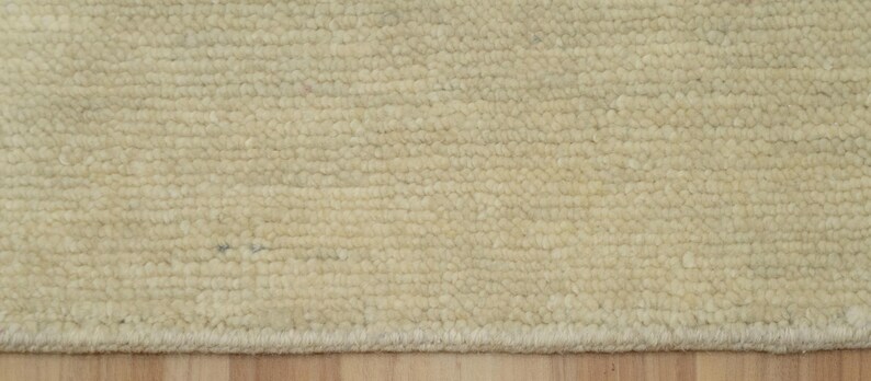 May include: A cream-colored rug with a dense, looped pile texture. The surface features a consistent, uniform pattern of small, rounded loops arranged in horizontal rows, creating a tactile and soft appearance across the entire visible area.