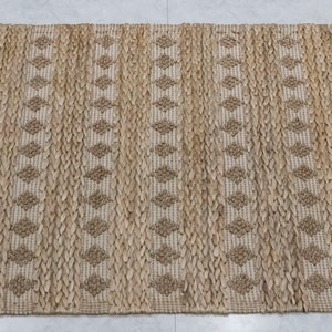 May include: A natural fiber rug with a woven diamond pattern in beige and brown tones. The rug is made of jute and has a natural, earthy look.