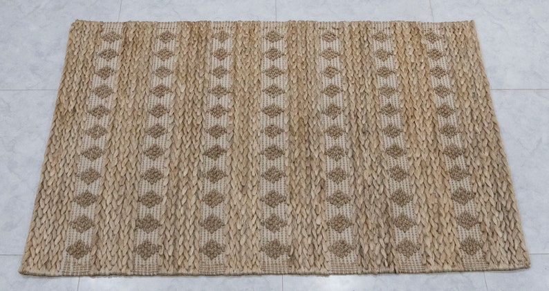 May include: A natural fiber rug with a woven diamond pattern in beige and brown tones. The rug is made of jute and has a natural, earthy look.