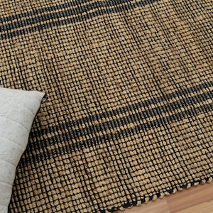 May include: A natural fiber rug with black stripes woven into the design. The rug is made of jute and has a natural, earthy look.