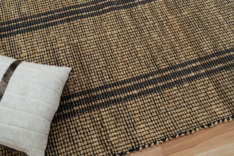 May include: A natural fiber rug with black stripes woven into the design. The rug is made of jute and has a natural, earthy look.