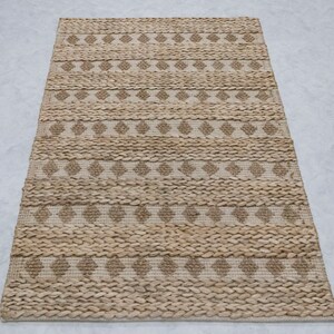 May include: A natural fiber rug with a woven diamond pattern in beige and brown tones. The rug has a rectangular shape and a textured surface.