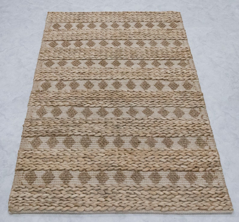 May include: A natural fiber rug with a woven diamond pattern in beige and brown tones. The rug has a rectangular shape and a textured surface.