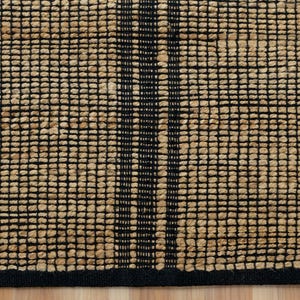 May include: A woven jute rug with a black and natural color pattern. The rug has a black border and a geometric design.