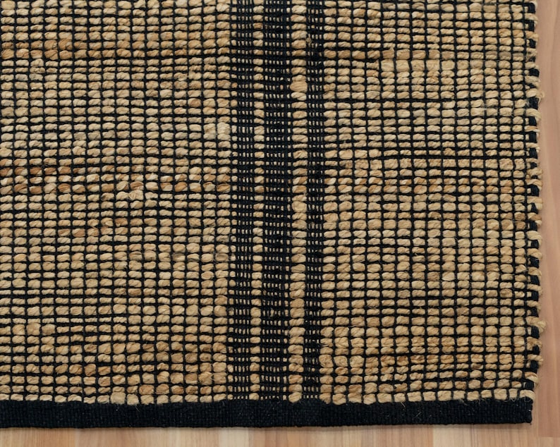 May include: A woven jute rug with a black and natural color pattern. The rug has a black border and a geometric design.