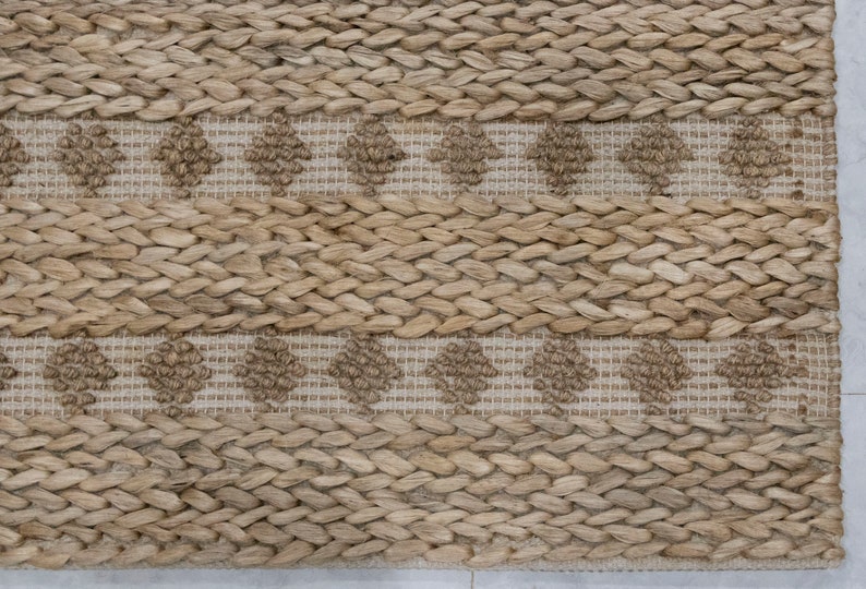 May include: A natural fiber rug with a woven pattern of brown and beige. The rug has a subtle diamond pattern in the center of the rug.