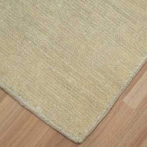 May include: A rectangular area rug featuring a solid cream-colored surface with a subtle, uniform ribbed texture. The rug has a clean, finished edge and a dense, tufted pile construction that covers the entire visible area of the floor covering.