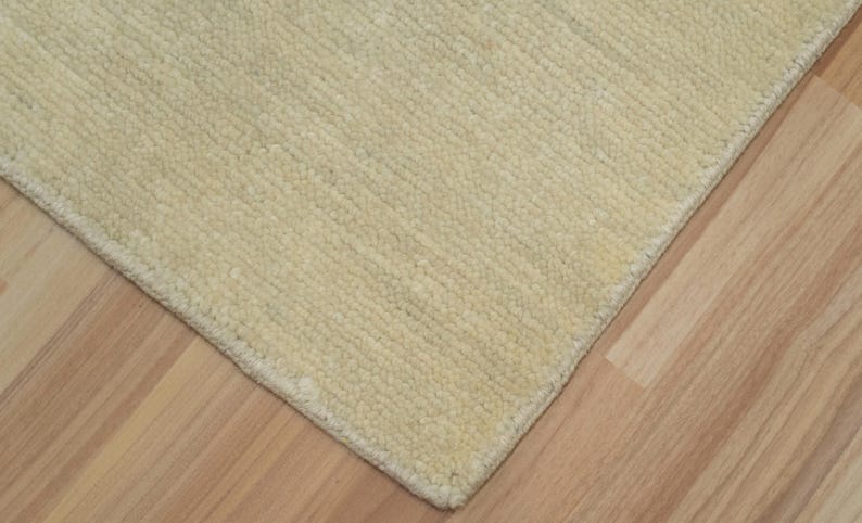 May include: A rectangular area rug featuring a solid cream-colored surface with a subtle, uniform ribbed texture. The rug has a clean, finished edge and a dense, tufted pile construction that covers the entire visible area of the floor covering.