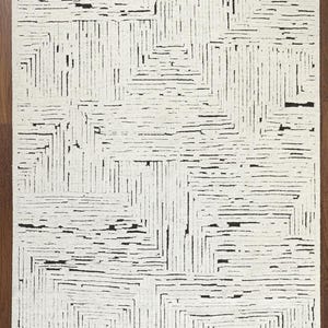 May include: Rectangular area rug with a geometric pattern. The rug features a white background with a repeating design of black lines and rectangular shapes. The rug is made of a soft material and is suitable for living rooms and bedrooms.