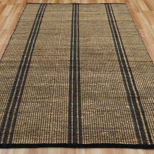 May include: A natural fiber rug with a woven texture and black stripes. The rug is made of jute and has a natural, earthy color.
