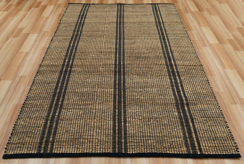 May include: A natural fiber rug with a woven texture and black stripes. The rug is made of jute and has a natural, earthy color.