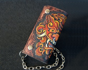 May include: A brown leather wallet with a chain attached. The wallet has a detailed orange and red illustration of a mythical creature with sharp teeth and horns.