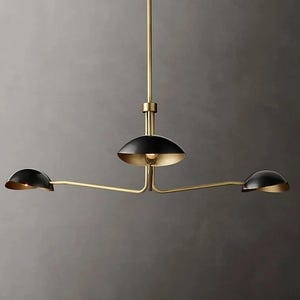 Op de afbeelding: Een gouden hanglamp met drie lampen en zwarte kapjes. De kapjes zijn rond en hebben een lichte bolling. De lamp heeft een eenvoudig, modern ontwerp.
