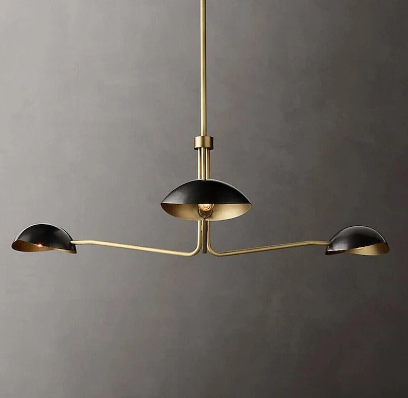May include: A gold three-light pendant chandelier with black shades. The shades are round and have a slight curve to them. The chandelier has a simple, modern design.