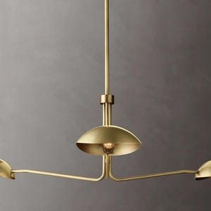 May include: A gold-toned three-light pendant light fixture with three round shades. The shades are angled and extend out from the center fixture.