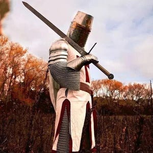 Puede incluir: Un caballero con armadura completa, vistiendo una t&uacute;nica blanca con una cruz roja, sostiene una espada a trav&eacute;s de su cuerpo. Est&aacute; de pie en un campo con &aacute;rboles en el fondo.