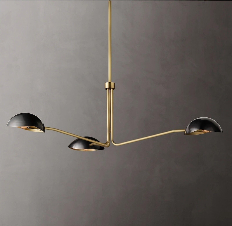 May include: A gold-toned three-light chandelier with black dome-shaped shades. The chandelier has a modern design with a simple, geometric shape.
