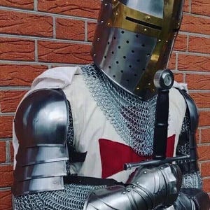 Puede incluir: Un caballero con armadura completa, lleva una cota de malla y un casco con una cruz roja en el pecho. Sostiene una espada en su mano derecha y tiene la mano izquierda en la cadera.