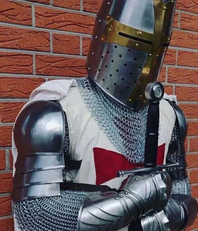 Puede incluir: Un caballero con armadura completa, lleva una cota de malla y un casco con una cruz roja en el pecho. Sostiene una espada en su mano derecha y tiene la mano izquierda en la cadera.
