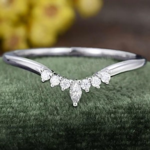 Puede incluir: Una delicada banda de boda curvada con un diamante de forma marquesa en el centro y diamantes redondos más pequeños a cada lado. La banda está hecha de oro blanco y tiene un acabado pulido.