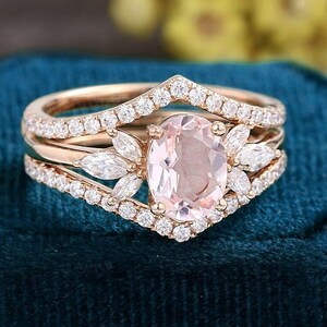 K&ouml;nnte beinhalten: Ein Verlobungsring-Set aus Ros&eacute;gold mit einem oval geschliffenen Morganit-Mittelstein und einem diamantbesetzten Band. Der Ring wird von zwei zus&auml;tzlichen B&auml;ndern begleitet, eines mit Chevron-Design und das andere mit einem Diamantband.