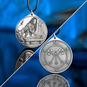 May include: A silver-toned circular pendant on a black cord. One side features an embossed lion standing over a figure on a stone slab. The reverse side displays a circular sigil with two crossed axes and the letters M, A, R, B, A, S arranged around.