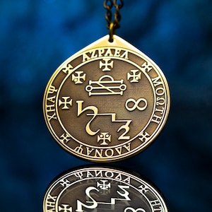 May include: A brass pendant with a circular design featuring a sigil, symbols, and the inscription "AZRAEL", "XNA", "HLTSOM", and "DHNOVV".