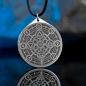 May include: Silver-colored pendant with a black leather cord. The pendant features an intricate design of alchemical symbols, including triangles, circles, and other geometric shapes. The pendant is circular with a triangular top.