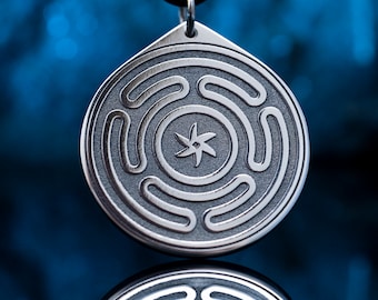 Puede incluir: Un collar con un colgante de plata de diseño circular que presenta una estrella de cinco puntas en el centro y círculos concéntricos a su alrededor.