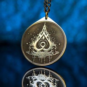 Peut inclure: Un collier avec un pendentif en laiton représentant un motif stylisé de flamme avec une goutte d'eau au sommet, entouré d'un motif tourbillonnant. Le pendentif est suspendu à une chaîne.
