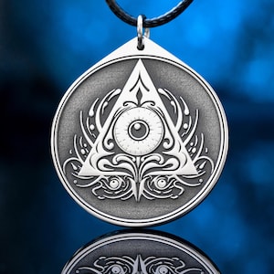 Peut inclure: Pendentif argenté représentant un œil dans un triangle, symbole souvent associé aux Illuminati. Le pendentif est suspendu à un cordon noir. Le design comprend des détails complexes et des ornements décoratifs.