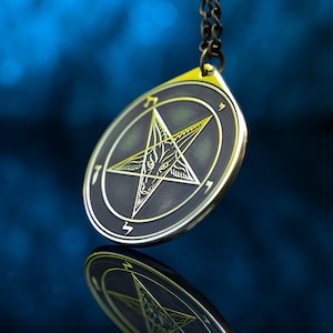 May include: A gold-colored pendant with a black background and a five-pointed star with a goat's head in the center. The star is surrounded by a circle with the number 7 on each point.