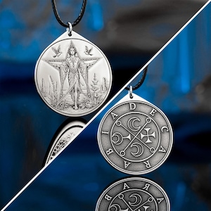May include: Two silver-colored pendants on black cords. One pendant features a figure within a star, with birds and a landscape. The other pendant has a circular design with letters and symbols. Both pendants are displayed against a blue background.