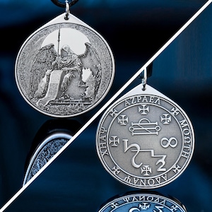 May include: Silver pendant with detailed engravings. One side depicts an angel with wings, holding a staff and scroll. The reverse side shows the word "AZRAEL" and other symbols. The pendant hangs from a black cord.