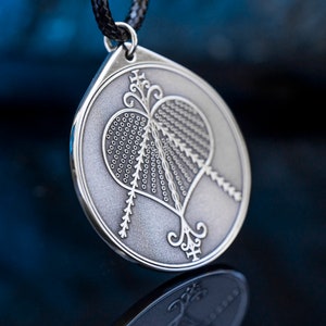 Könnte beinhalten: Eine silberne Halskette mit einem herzförmigen Anhänger, der mit komplizierten Details und einer strukturierten Oberfläche verziert ist.